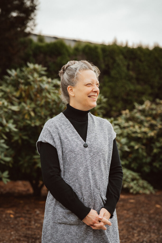 Julie, blog author, smiling with squinted expression in the outdoor light of a cool autumn morning with green shrubs in the background